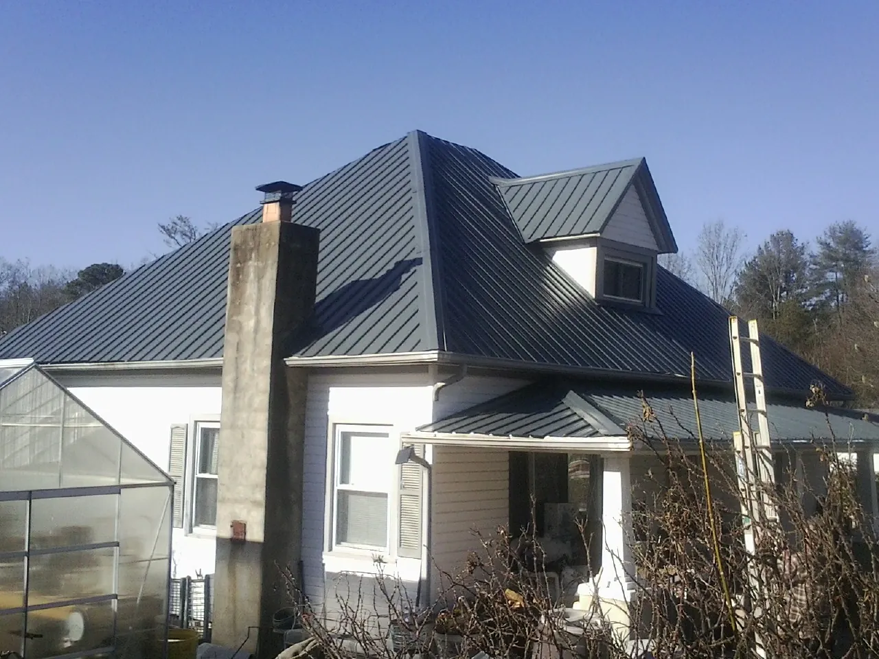 Dark blue standing seam metal roof on a white farmhouse with dormer — Slate & Tile Roof Repair by Roofing Brothers in Coal Center