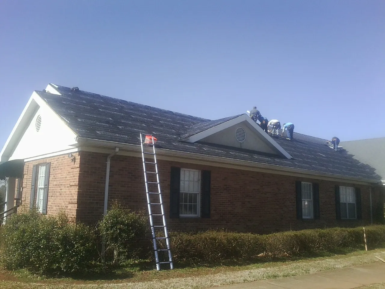 Crew tearing shingles off a brick ranch roof with a ladder set — Metal Roof Repair work by our crew in Coal Center