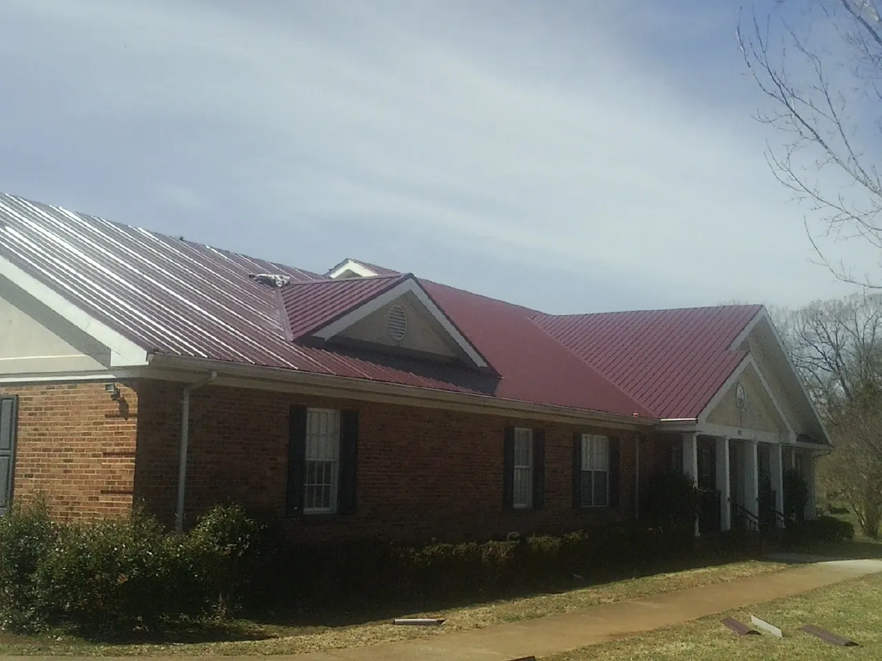 Red metal roof with gabled entries on a long brick building, from a Hail Damage Roof Repair job in Coal Center