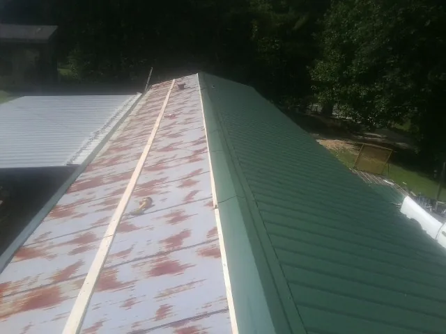 Old rusted panels beside newly installed green metal roofing — Wind Damage Roof Repair by Roofing Brothers in Coal Center