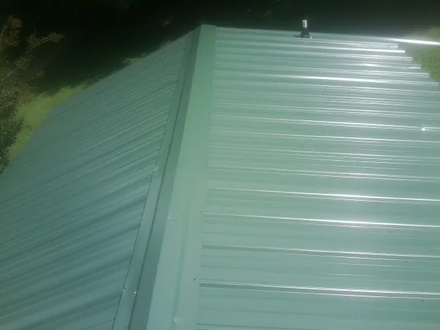 New green metal panels meeting at the ridge of a roof — Flat Roof Repair work by our crew in Coal Center