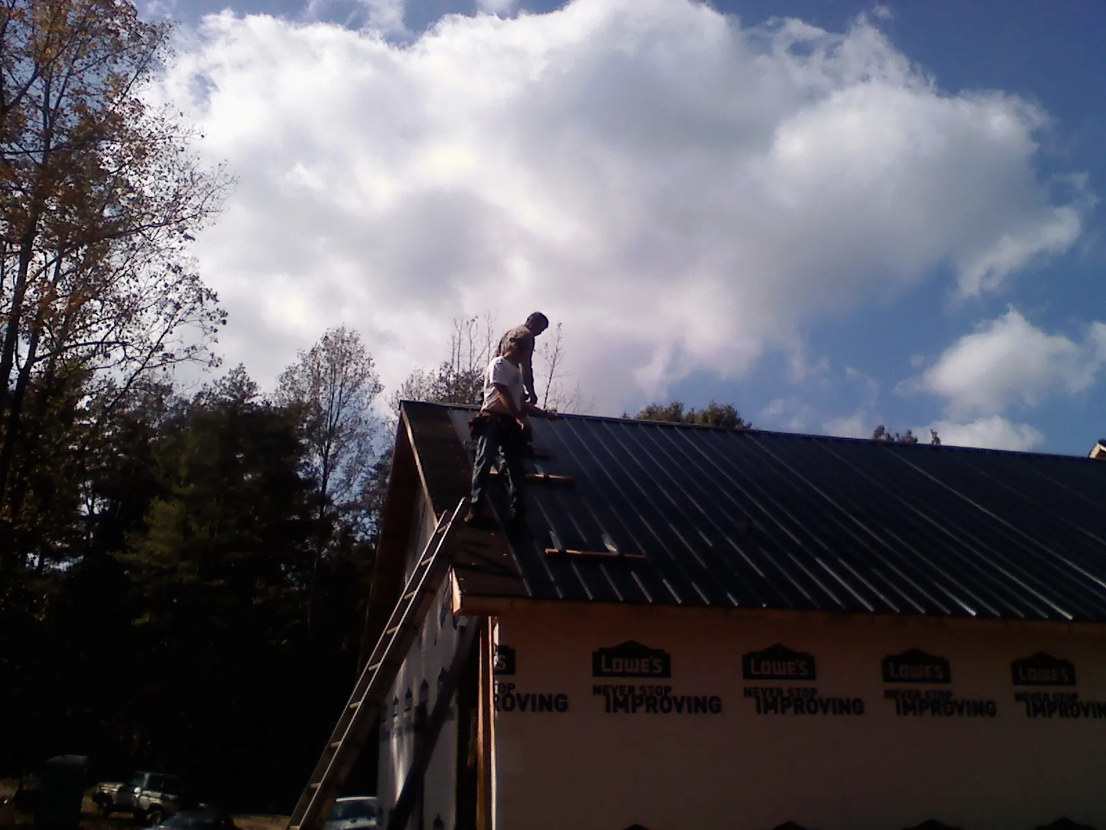 Roofer fastening dark metal panels high against a cloudy sky, from a Roof Inspection job in Coal Center