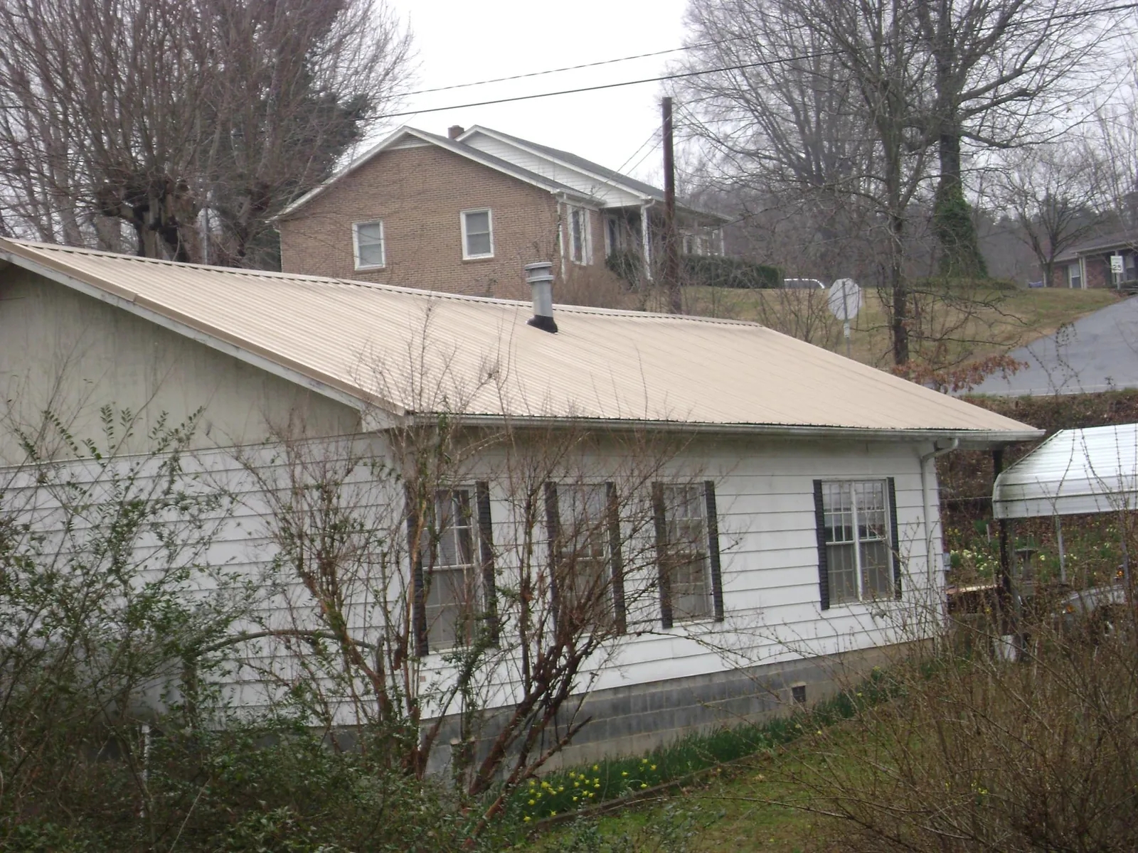 Tan metal roof on a white sided house set into a hillside — Commercial Roofing by Roofing Brothers in Coal Center