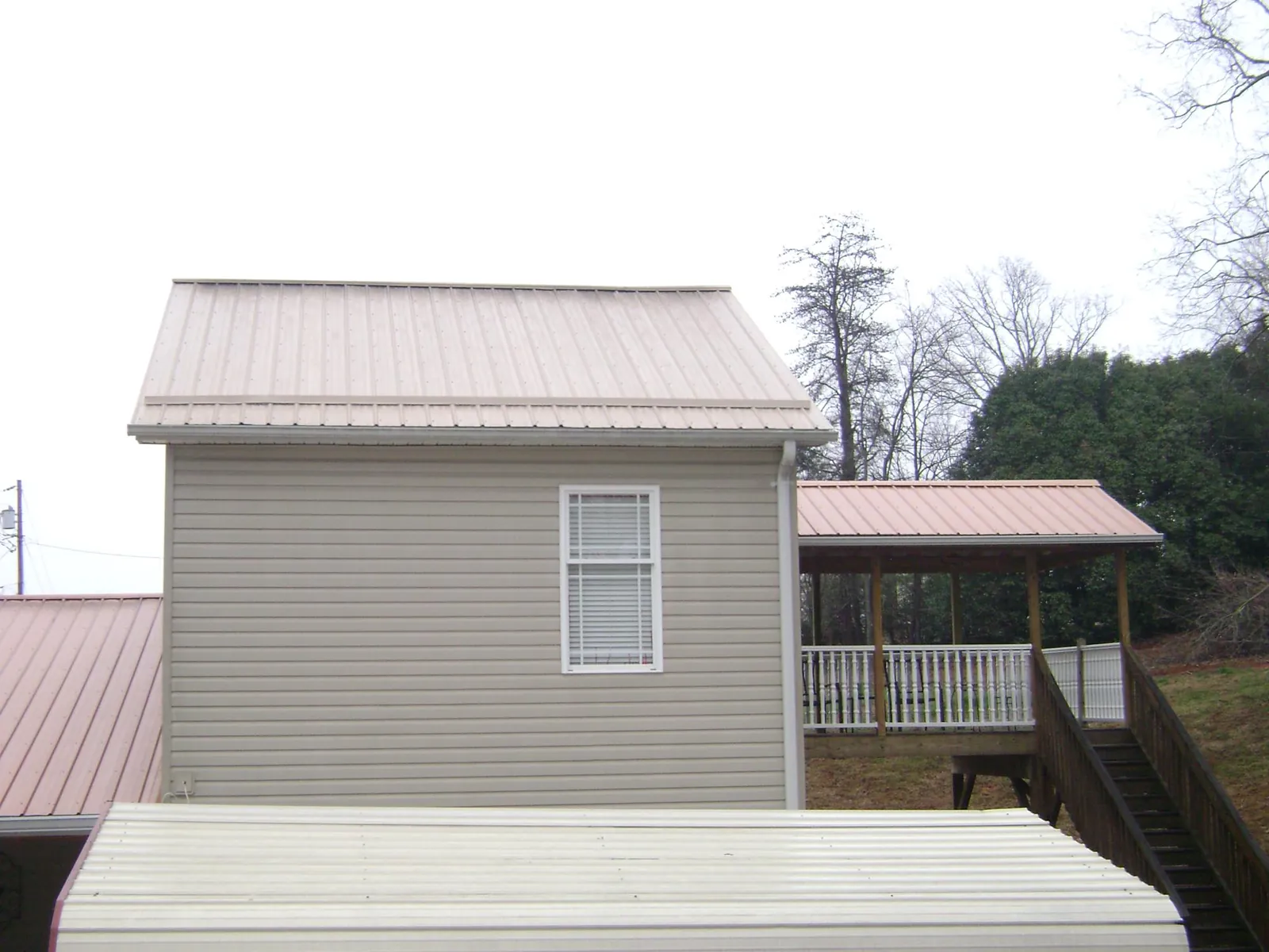 Tan metal roofs on a two story addition and attached porch, from a Roof Replacement job in Coal Center